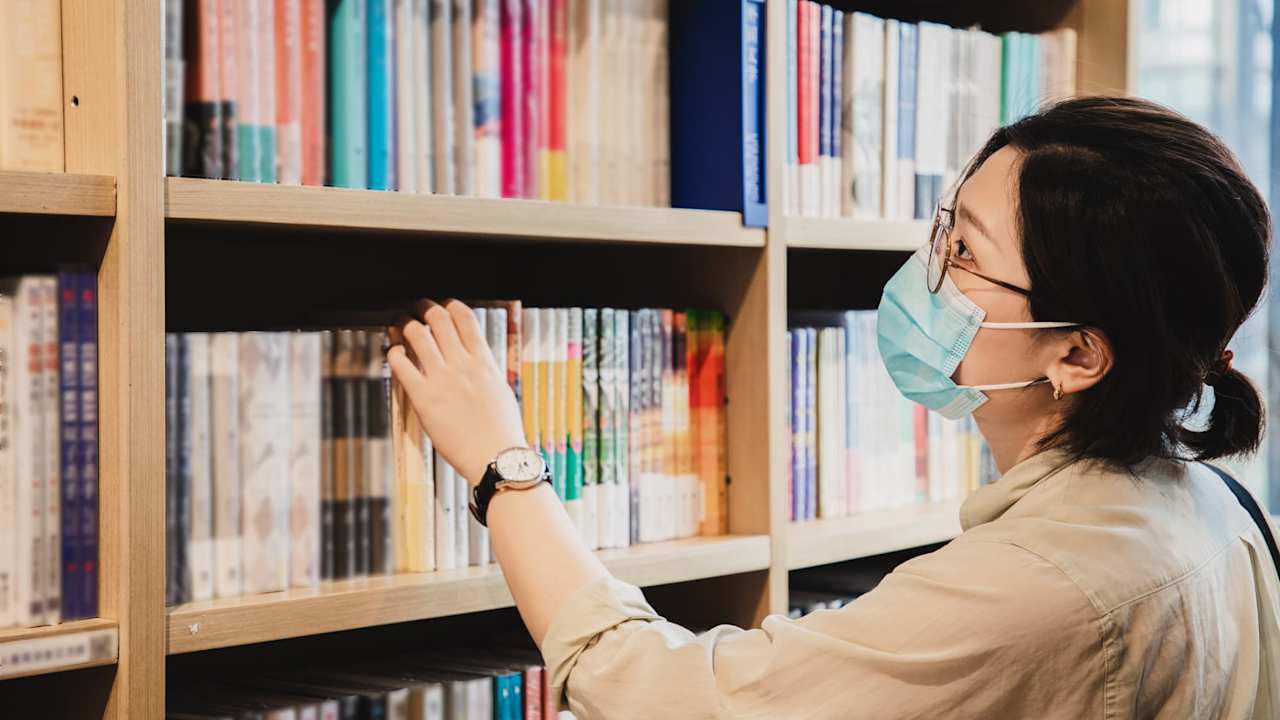 Female college student chooses a book from the college library.