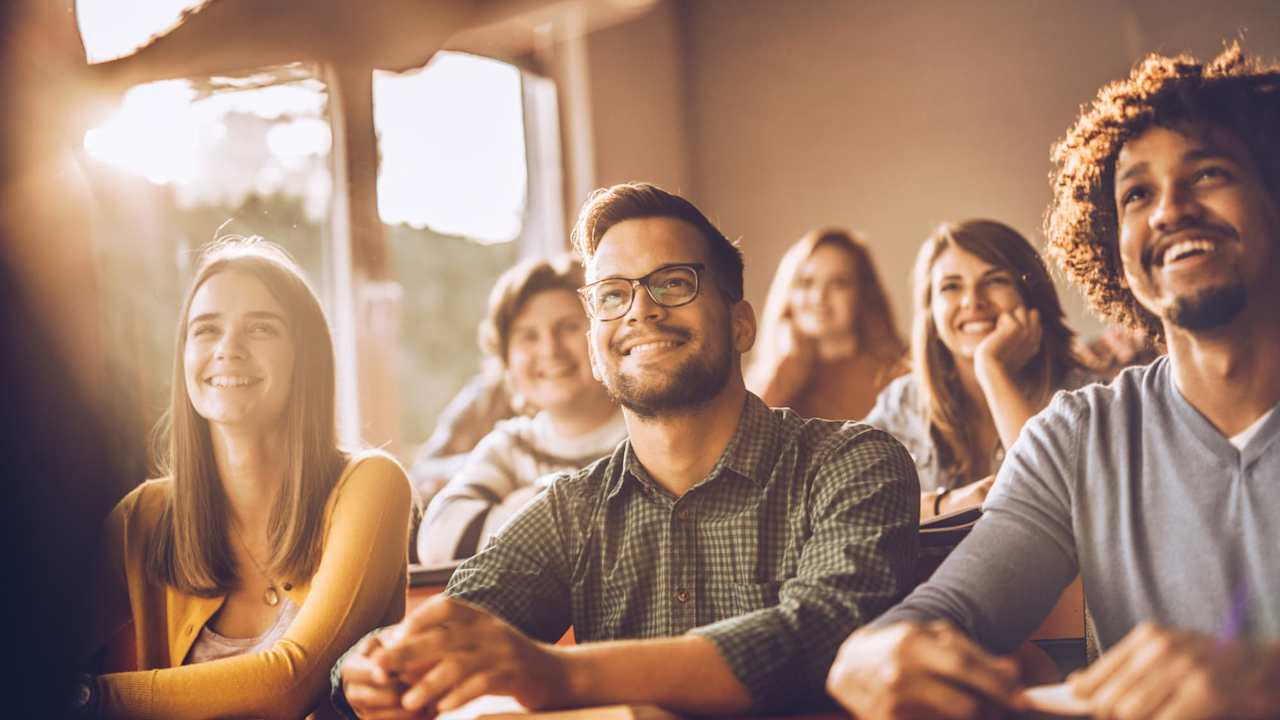 Group of happy students listening to a professor speaking during class.