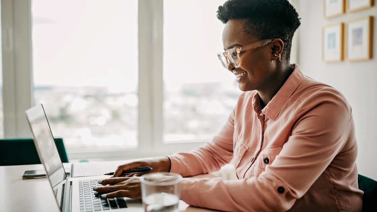 A woman working from home on her laptop. She is sitting at her desk by a big bright window.