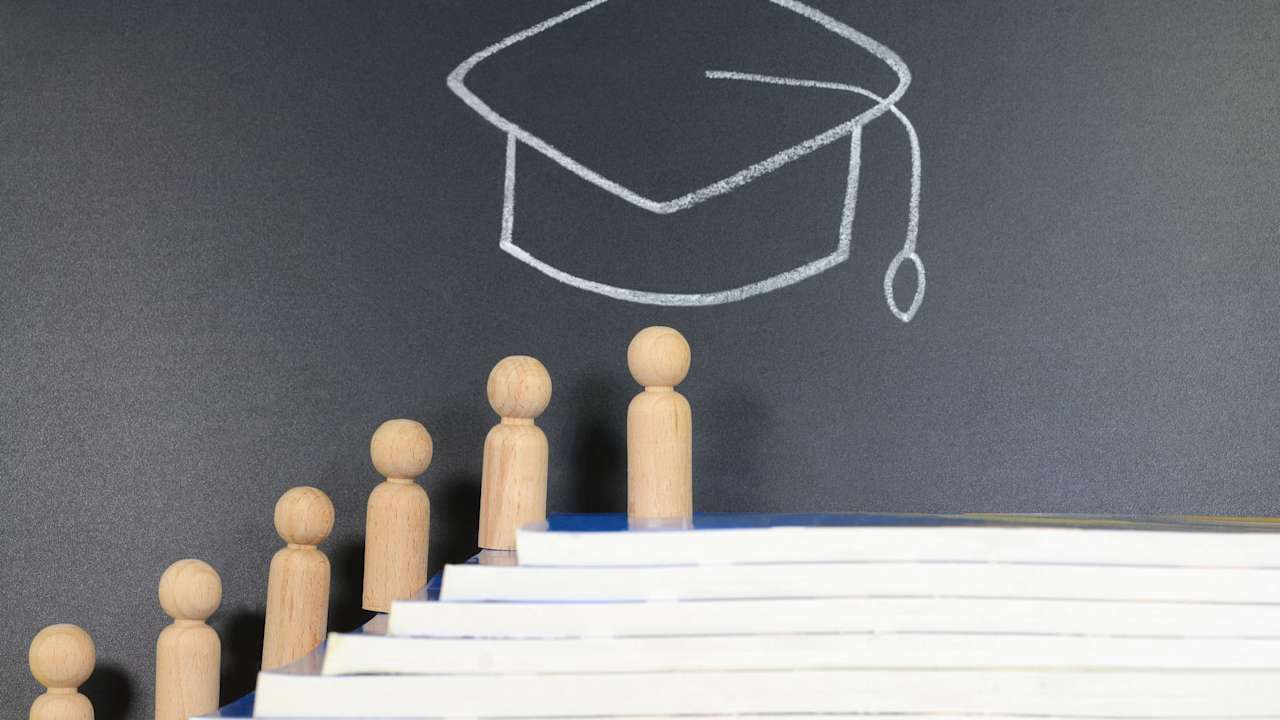 Concept of Graduation. Wooden figurine climbing on top of stacked books with graduation hat drawing on the background.