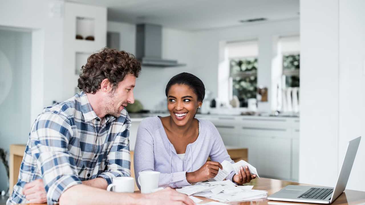 Happy multi-ethnic couple paying bills on laptop at home