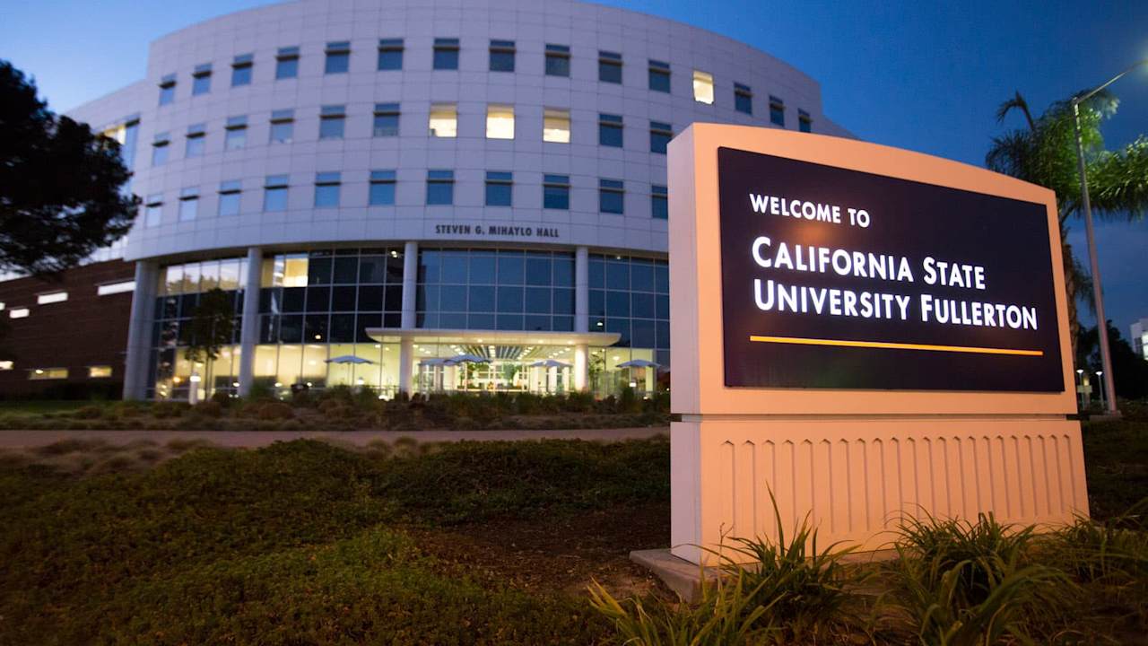 Campus sign for California State University Fullerton and building at dusk