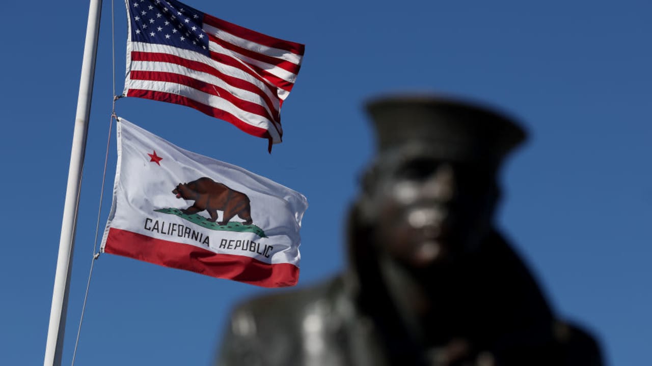 An American flag and the California State flag flying next to the Lone Sailor statue in Sausalito, California.