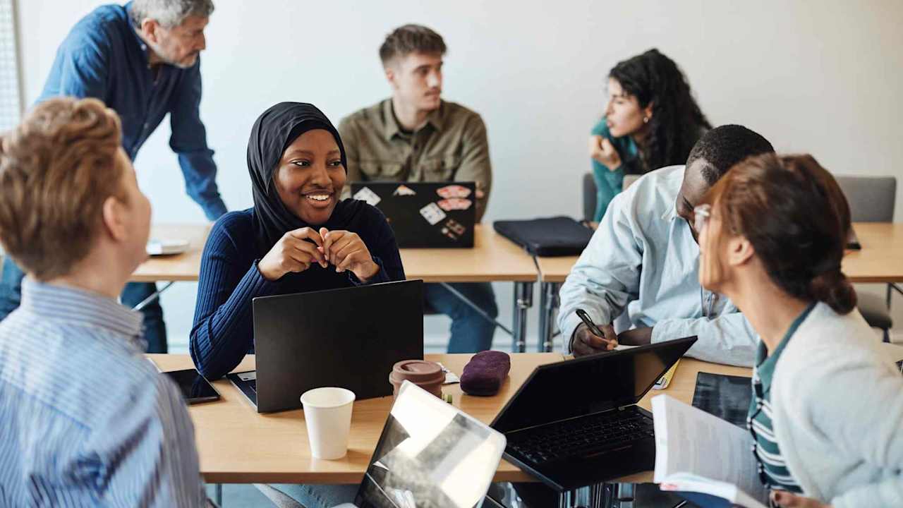 Smiling Black female college student wearing a hijab head covering having a discussion with friends while sitting in a classroom on campus.
