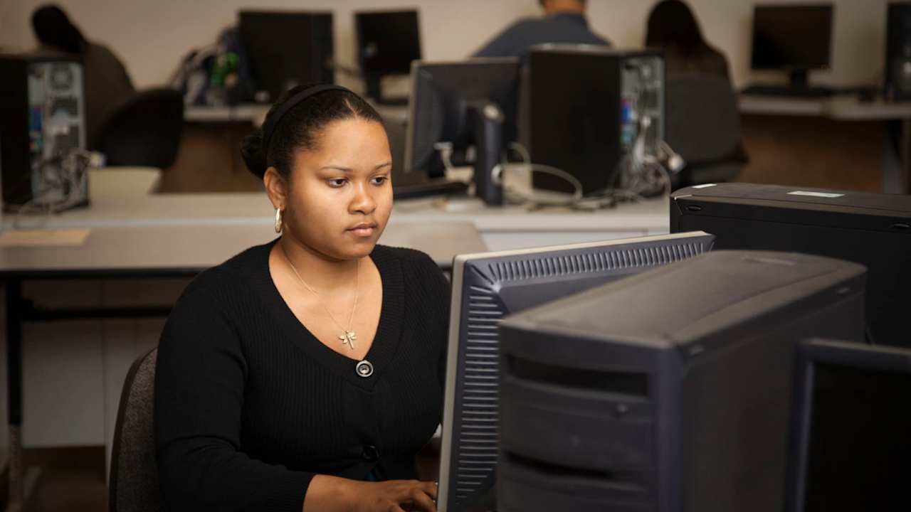 Black female student typing on a desktop computer in a community college computer lab.