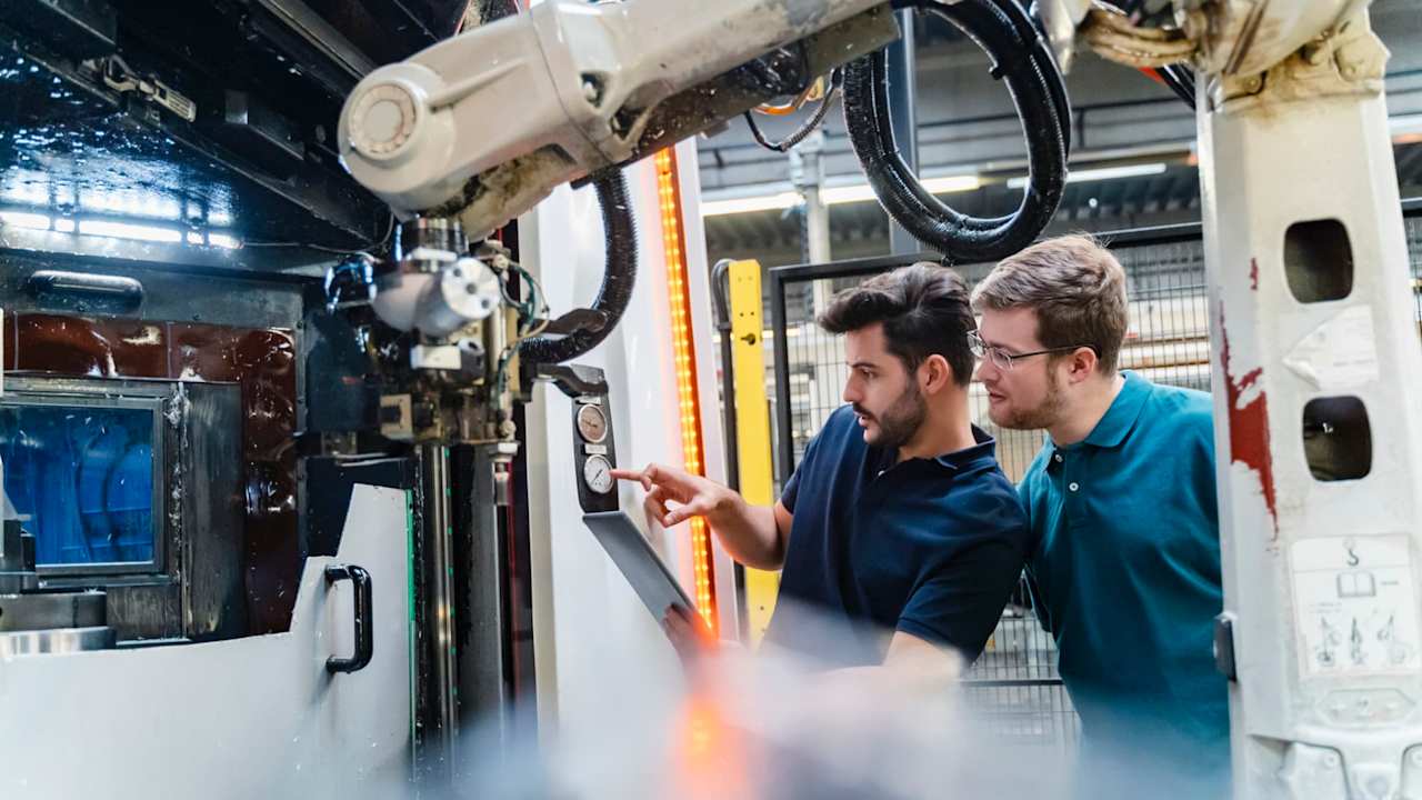 Male coworkers using digital tablet while examining robotic arm at manufacturing factory