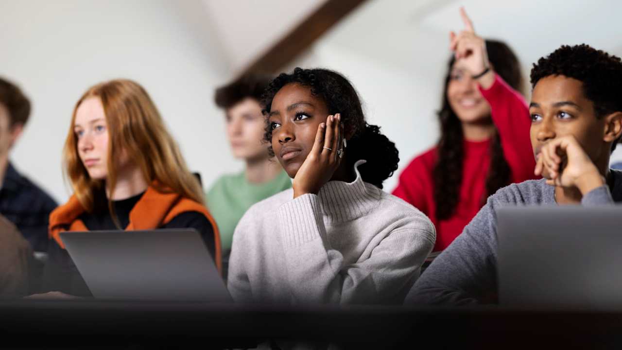 A group of high school students listening to their teacher in a classroom.