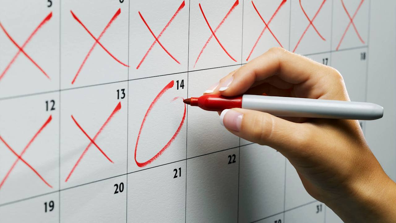 Close up of a college graduate using a red sharpie pen to mark off days on a calendar until she pays off her student loans.