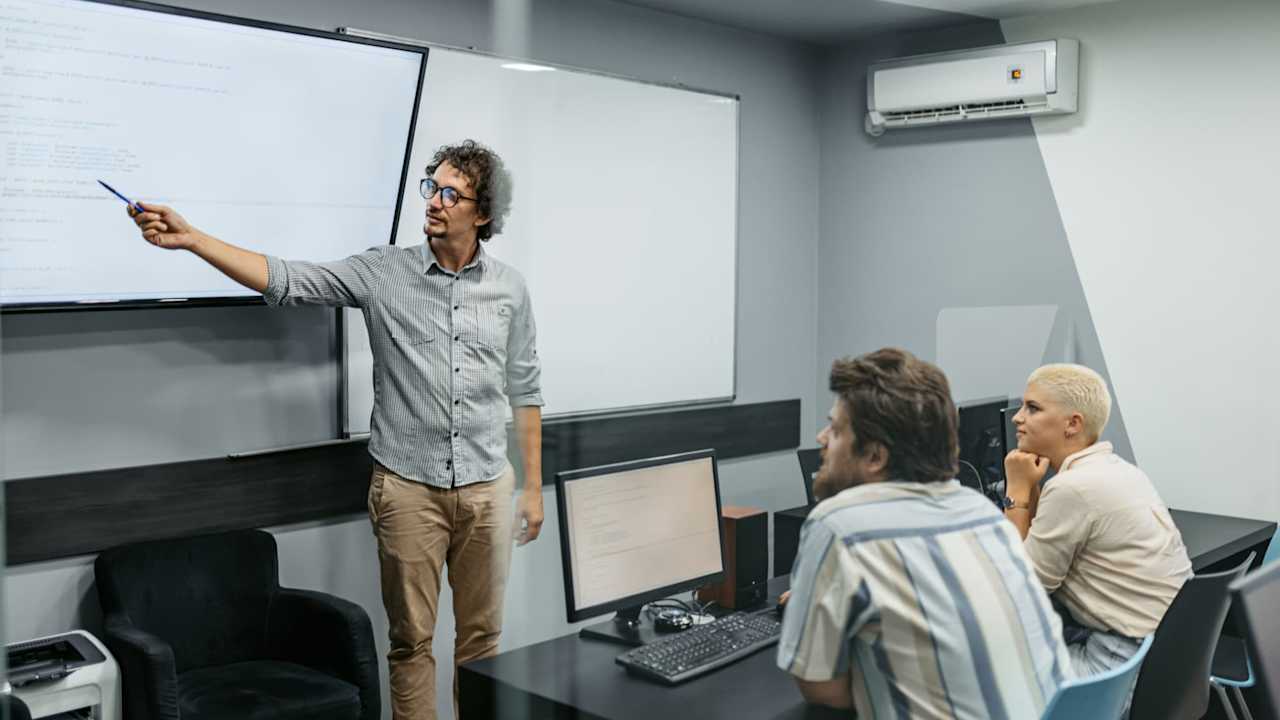 Young male teacher teaching young students a programming class in the classroom.