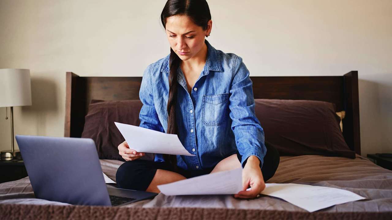A woman sitting on her bed in a home looking through finances.