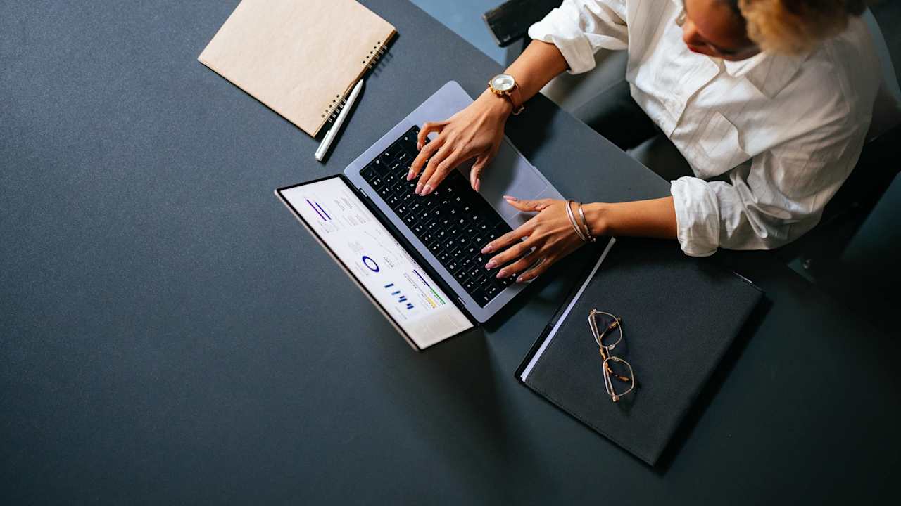 High Angle View Of Unrecognizable Woman Typing Business Report On A Laptop Keyboard In The Cafe