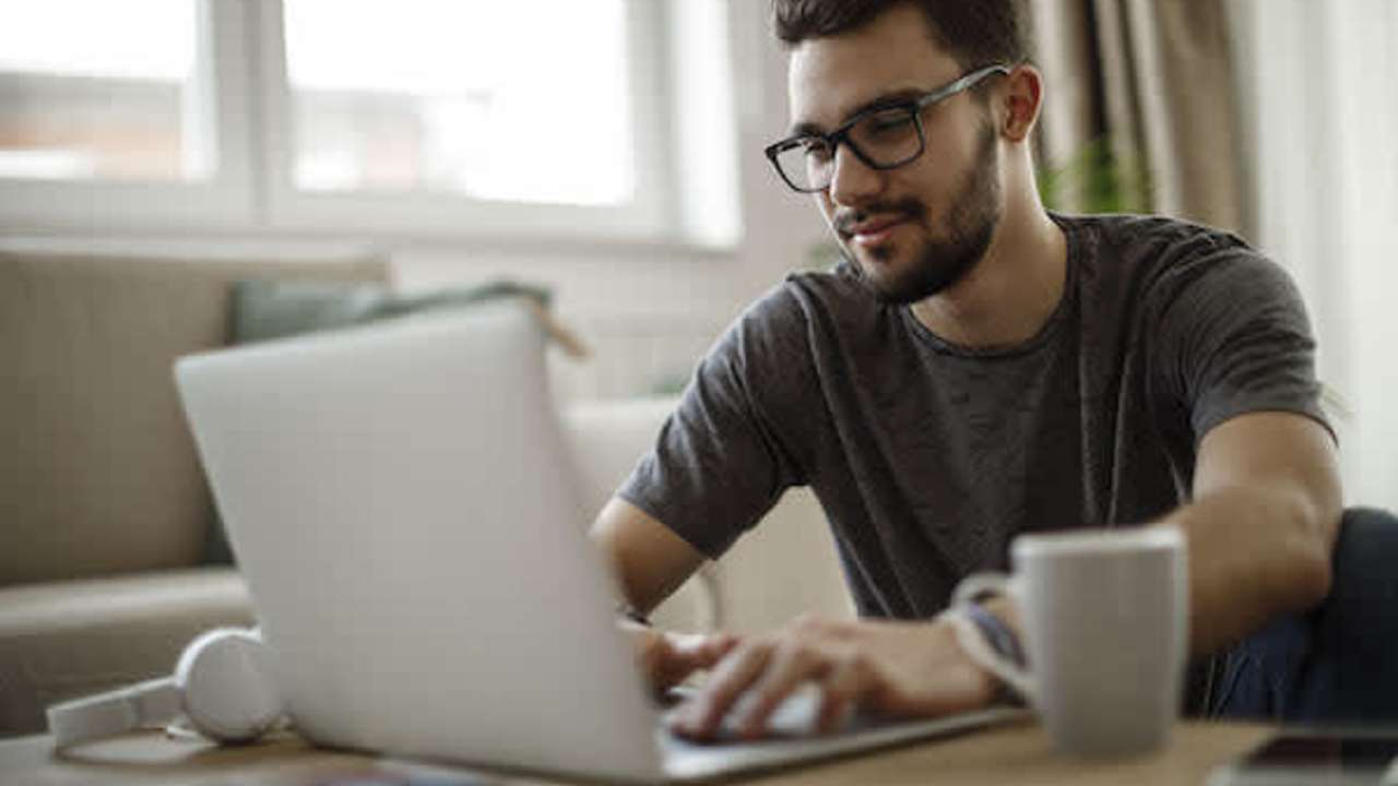 Man working on his laptop with a cup of coffee next to him on his desk