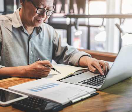 Person on laptop with a chart and calculator beside them
