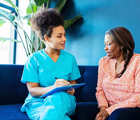 Mid-adult Black female nurse talking with her senior patient while taking notes