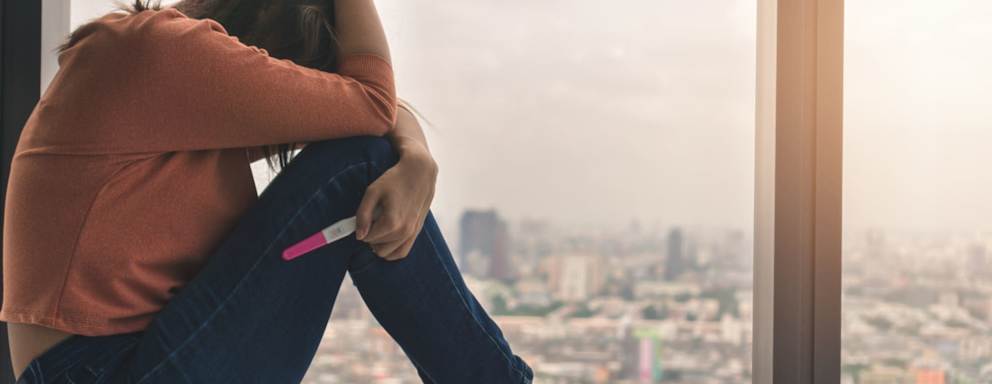 Unhappy young asian woman holding pregnancy test showing a negative result and sit down near big window city view on evening time, Wellness and healthy concept, Infertility problem, Selective focus.