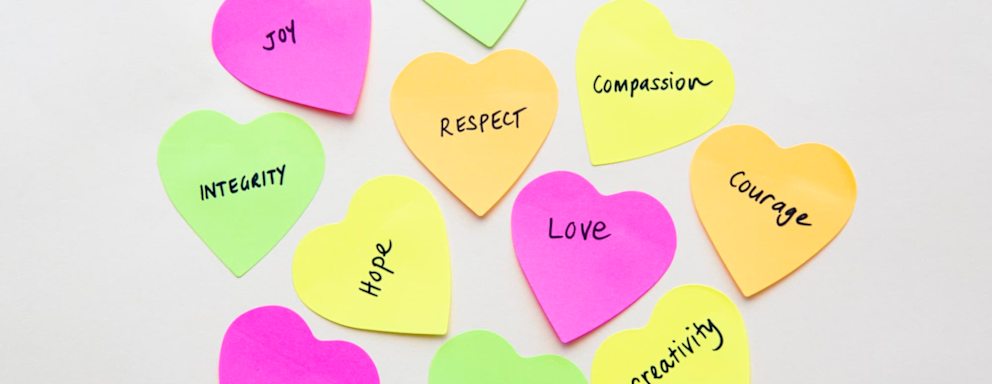 Values such as courage, justice, and creativity handwritten on heart shaped sticky notes.
