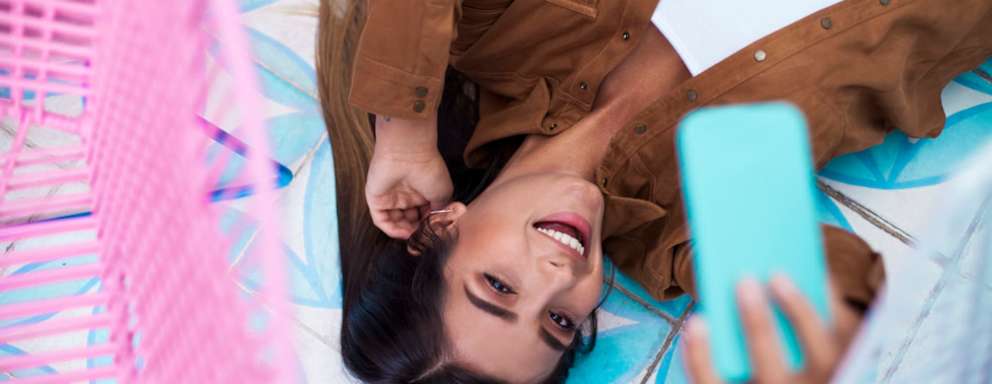 College student watches TikTok videos on her mobile phone while lying on her dorm room bed.