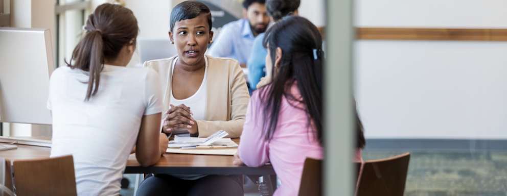 Mom and her college-aged daughter talk with a university financial aid employee about applying for a HEERF grant.