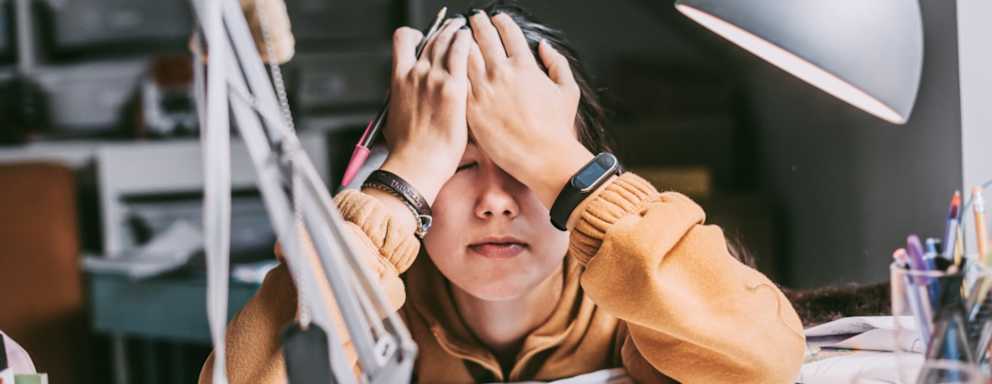 Stressed out high school student sitting at her bedroom desk at home with her head resting against her forehead in a moment of frustration.