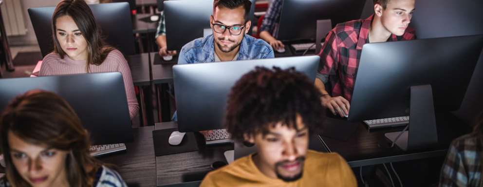 Large group of high school students in a classroom use desktop computers to take a standardized test.