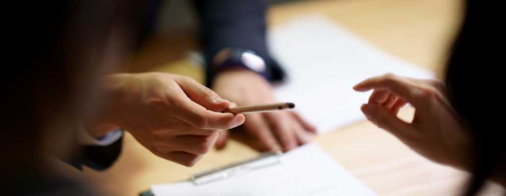 Loan agent handing a pen to a college student to sign contract agreement papers.