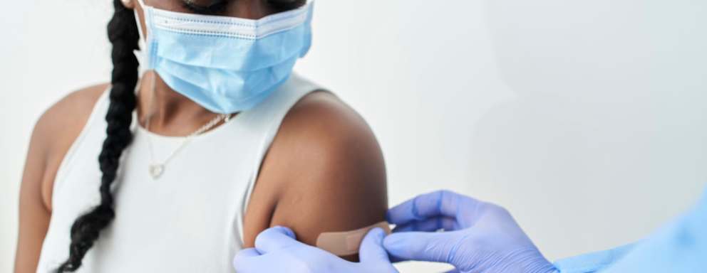 Nurse or doctor putting an adhesive bandage on the arm of a black woman after administering the covid19 vaccine.