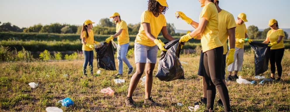 A large group of people wearing yelow shirts and hats, picking up trash in a big field.