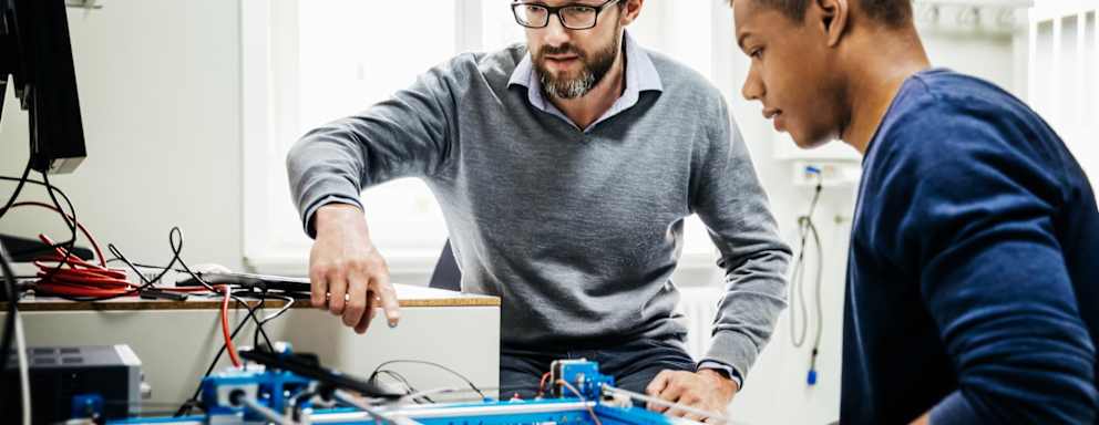 An engineering tutor assisting one of his students with a technical problem during teaching session at university.