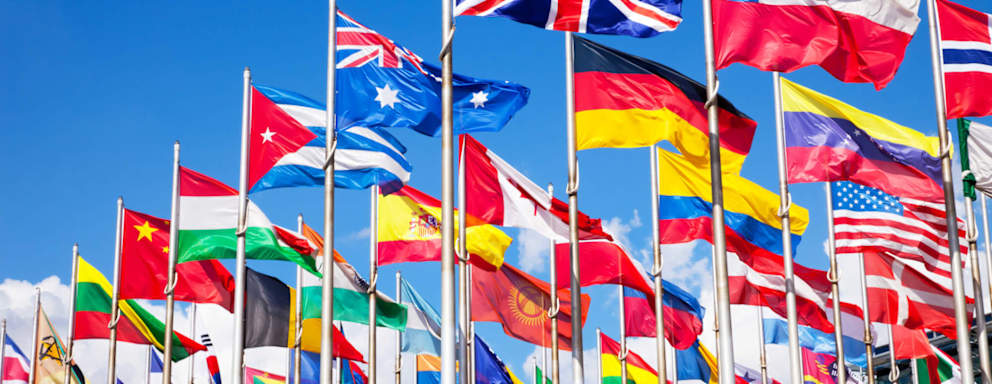 A series of flags from international countries sway in the wind in front of a college campus building. American colleges and universities are beginning to accept international students following enrollment declines during the COVID-19 pandemic.