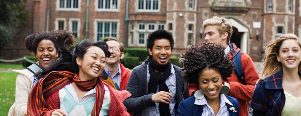 Excited university students smiling and laughing for a photo in front of a building on a campus