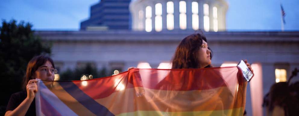 Transgender rights advocates hold pride flags during a rally against Ohio legislation banning transgender women from female sports.