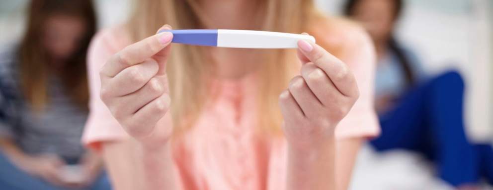 Teenage girl with pregnancy test in hand, reading the results.