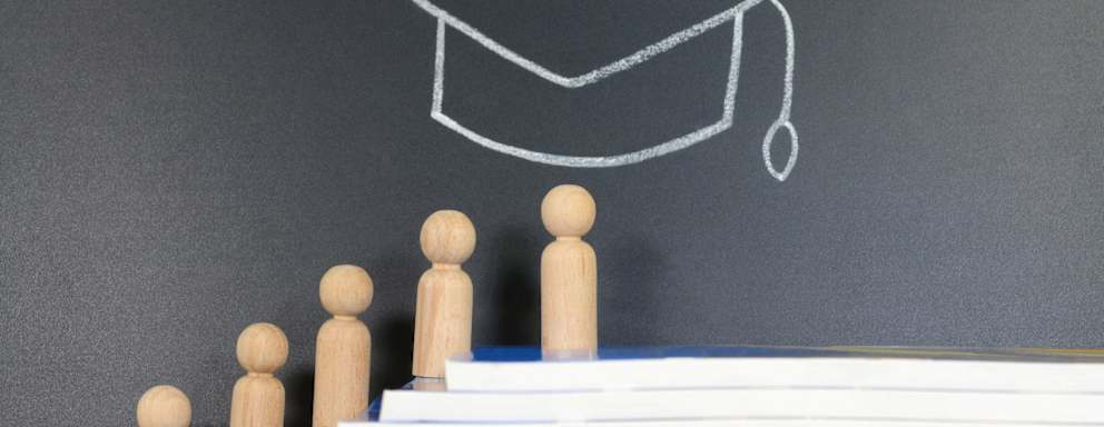 Concept of Graduation. Wooden figurine climbing on top of stacked books with graduation hat drawing on the background.