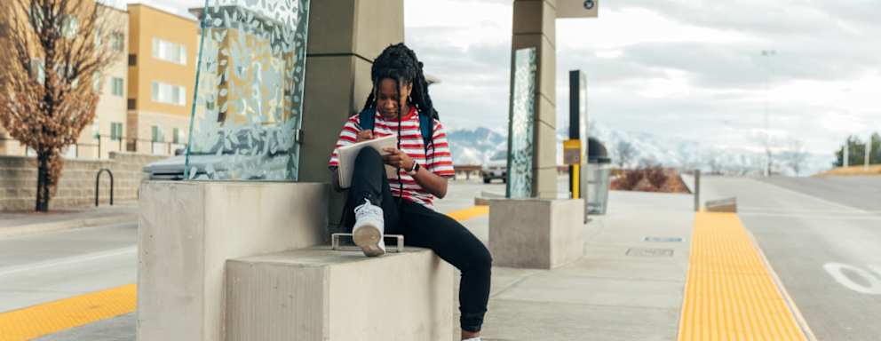 A female college student is at a bus stop waiting for the next bus.