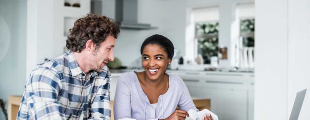 Happy multi-ethnic couple paying bills on laptop at home