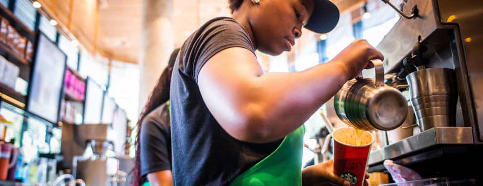 A Starbucks barista pours steamed milk into a beverage inside a cafe. Full- and part-time Starbucks employees can attend Arizona State University online for free through the company's College Achievement Plan.