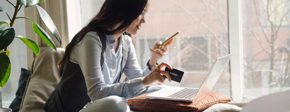 College student sitting on her bed in front of her laptop uses her credit card to pay an online bill.