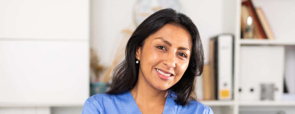 Latina nurse greeting patients in a medical office, filling out forms on a clipboard. Image Credit: Iakov Filimonov / Shutterstock