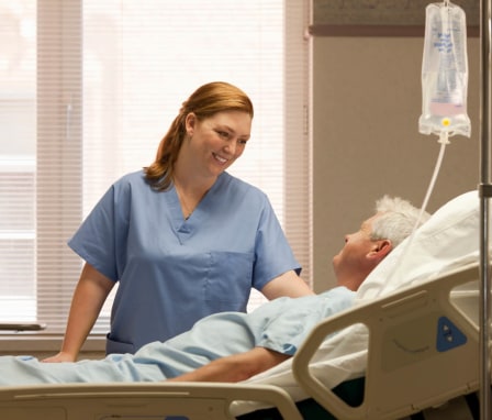 Smiling mid-adult female nurse checking in on an elderly male patient by his bedside in a hospital room