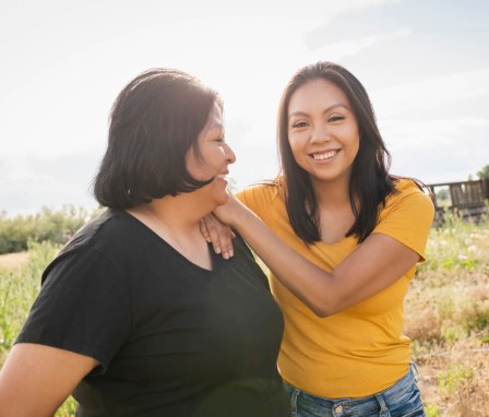 Native American mother and her adult daughter smile while walking outside in a rural area.