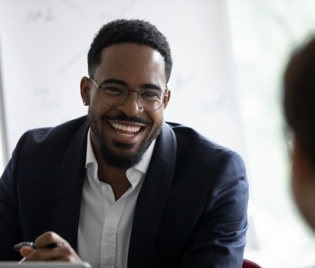 African-American male recruiter dressed in business attire. He is sitting in an office chatting with a job-seeker.