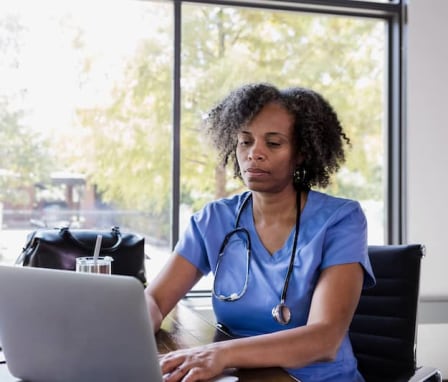 Nurse typing on laptop beside window