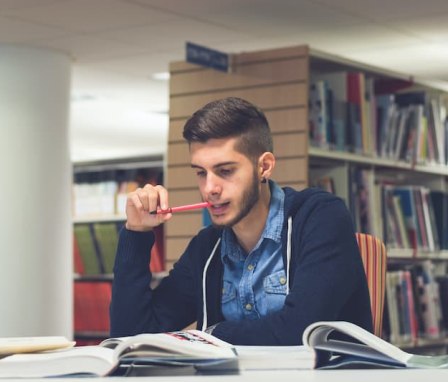 Young man studying textbook in library