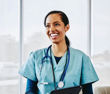 A young African-American female nurse smiling while standing in a hospital lobby.