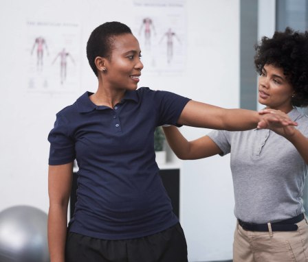 A Black female physical therapist is helping her senior patient with arm exercises during a physical therapy session.