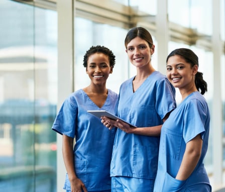 A diverse group of female nurses looking at data on a digital tablet in a hospital.