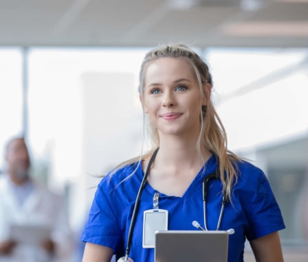 Young female medical assistant walking through a hospital hallway, holding a patient's file in her hand.