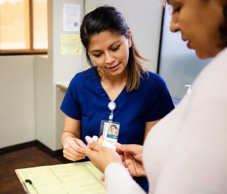 A mid-adult Hispanic female nurse is chatting with a physician behind the administrative desk of the clinic. She is holding a patient file in her left hand and consulting with the physician about the patient's medication.