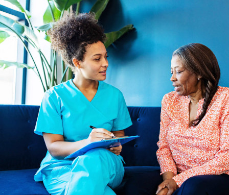 Mid-adult Black female nurse talking with her senior patient while taking notes