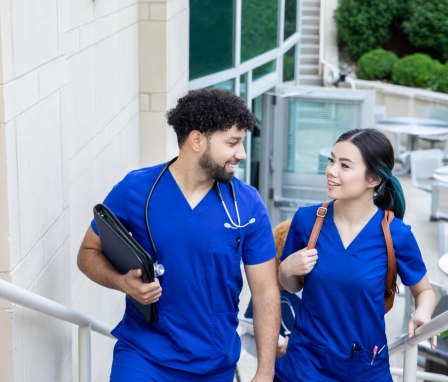 A pair of nursing students (one male and one female) are chatting while walking to class together on campus.